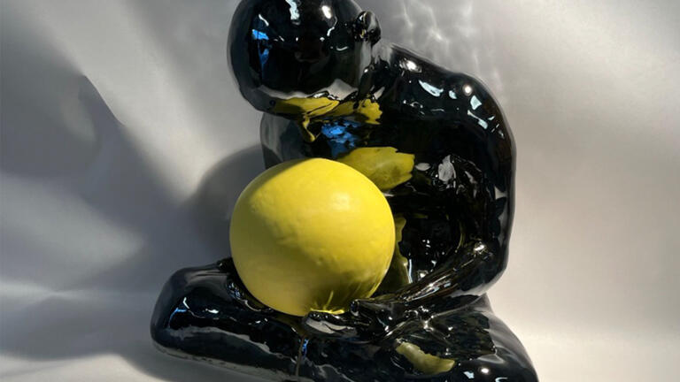 Glossy black sculpture of a seated figure holding a bright yellow sphere