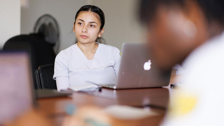 student in white scrubs sits in class