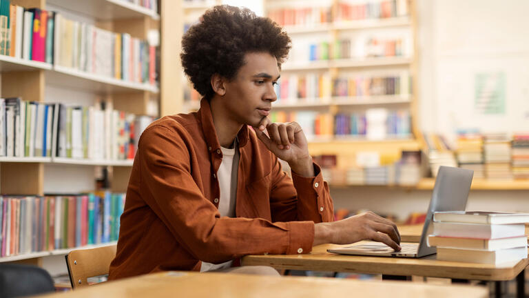Young professional working on laptop in a library, surrounded by books