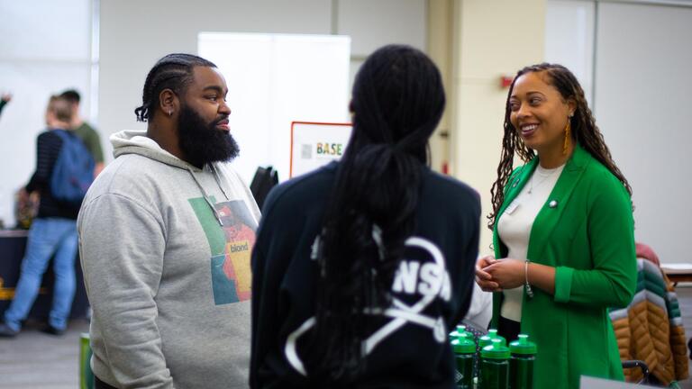 2 students talking to a representative at a tabling eventf