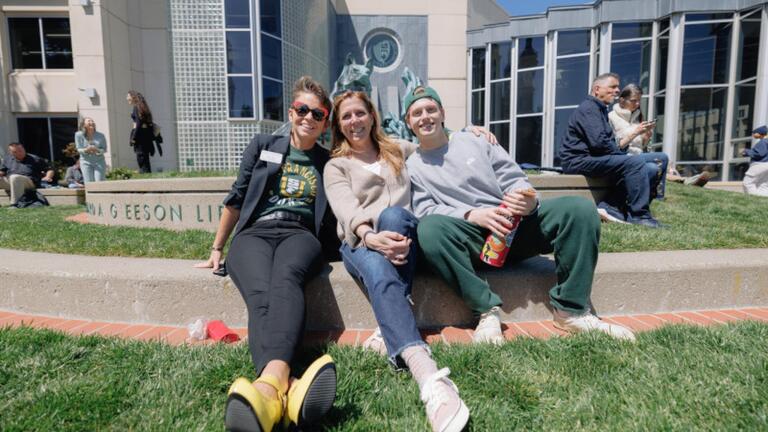 3 students sitting on the grass in front of Gleeson library
