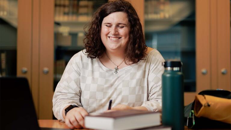 Person sitting at a table with books, a water bottle, and laptop