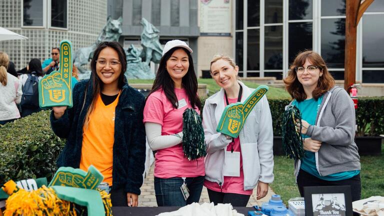 four students standing behind a table and holding USF gear