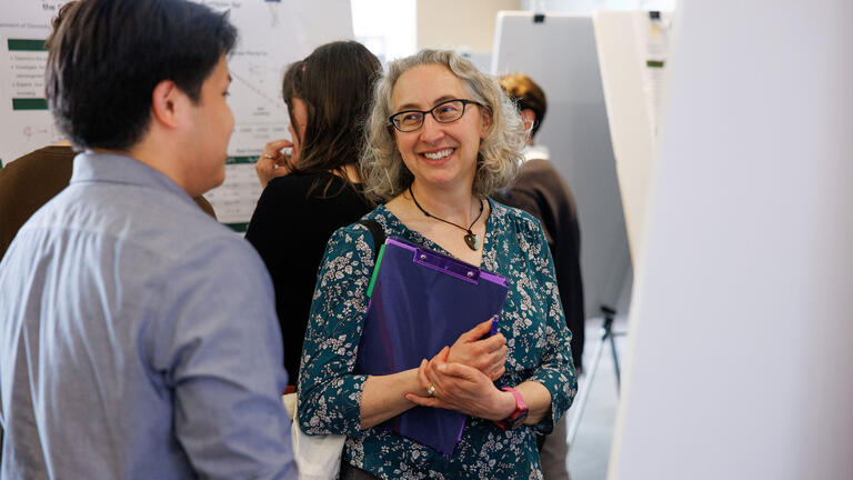 Student carrying a folder, chatting with another student
