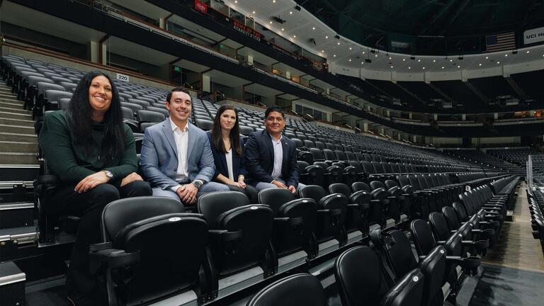 Four sport management students sitting in indoor stadium seats, smiling