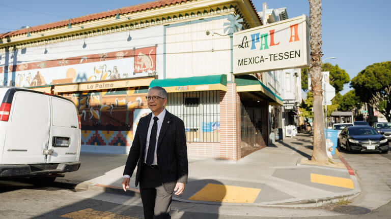 President Aceves walking in the mission in front of a corner store