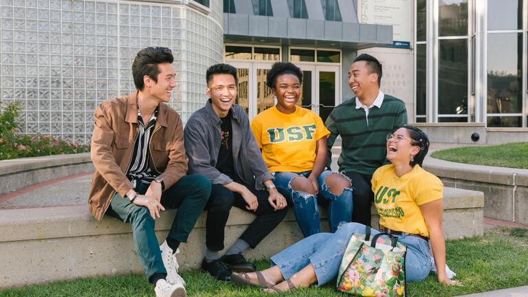 group of USF students sitting outside on the ground and laughing