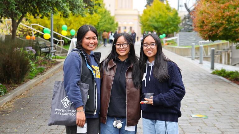Three students posing, smiling on campus