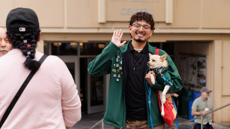 Student waves hand in the air while holding a small dog