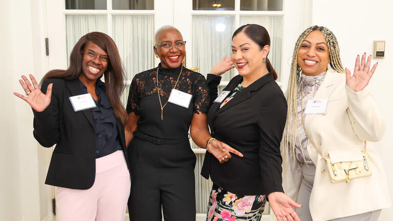 Group of four women posing and smiling with their hands up