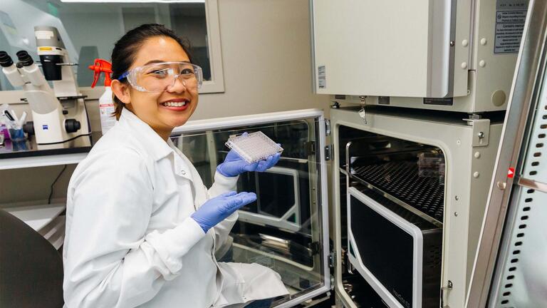 Student in science lab wearing gloves, goggles, and a lab coat