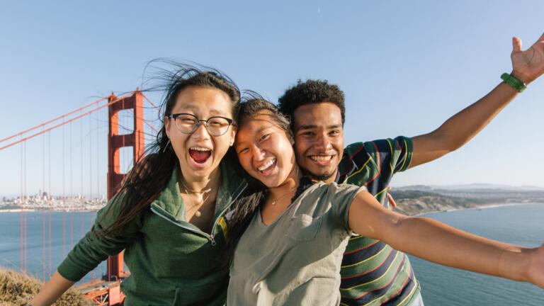 Three students at golden gate bridge smiling.