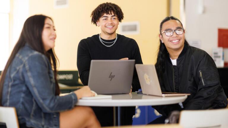 Three students at a table smiling 
