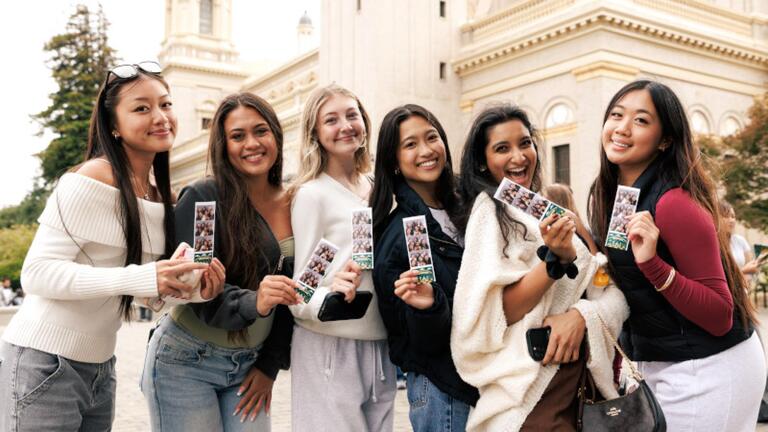 Six students holding up photos while smiling.