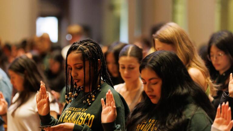A group of students raises their right hands while reciting the New Student Pledge during New Student Convocation.