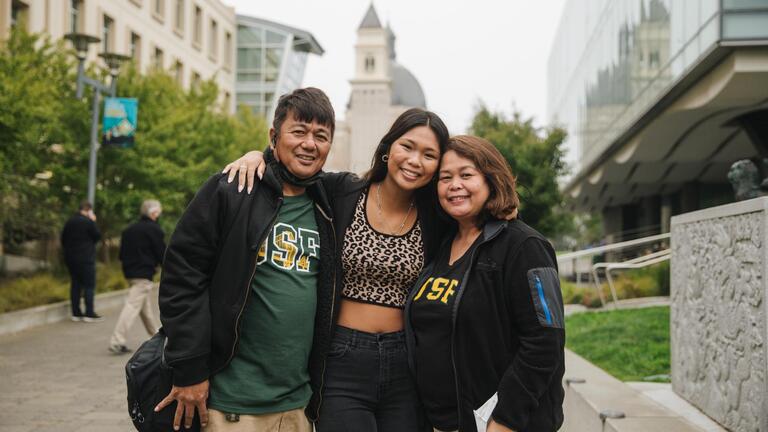Three family members smiling with church in the background.