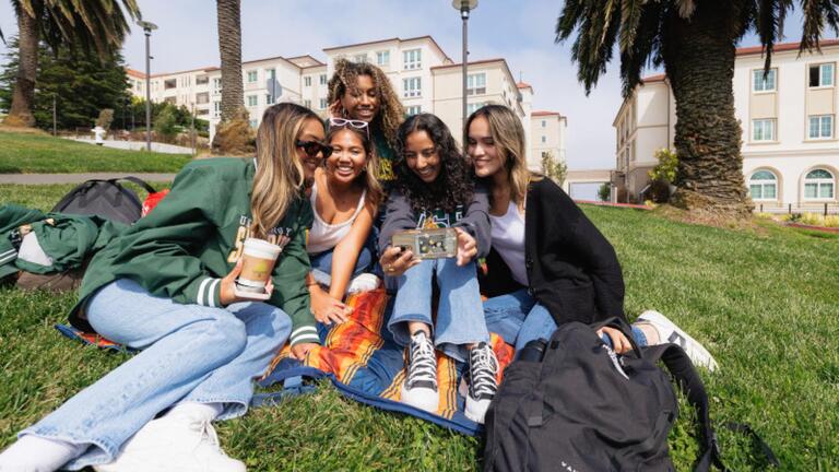 Five students looking having a picnic and smiling.