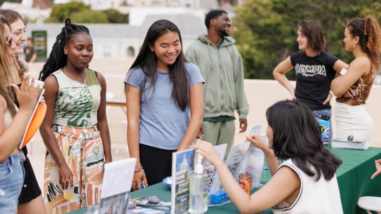 Students speaking with a woman sitting a table promoting a program