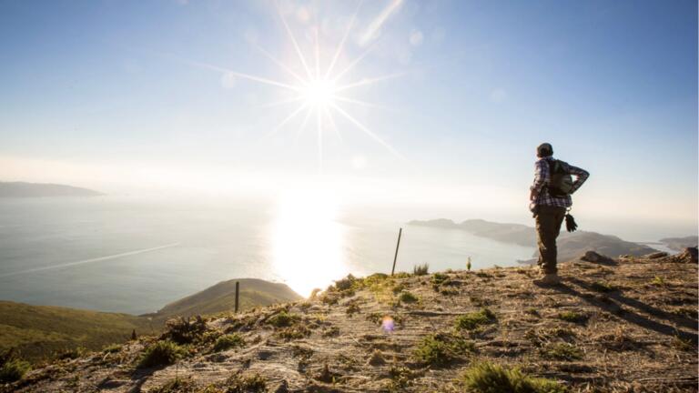 Person standing at the top of a mountain top looking off to the San Francisco Bay