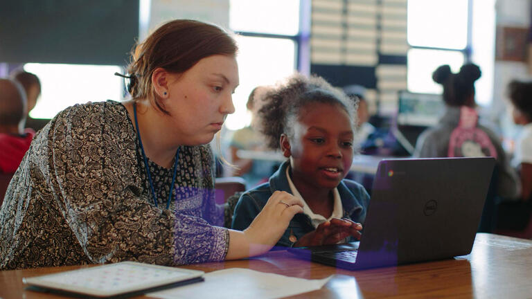 Teacher and student look at a laptop computer