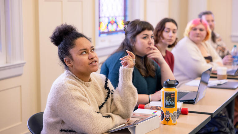 Student seated next to peers in classroom speaking aloud to class