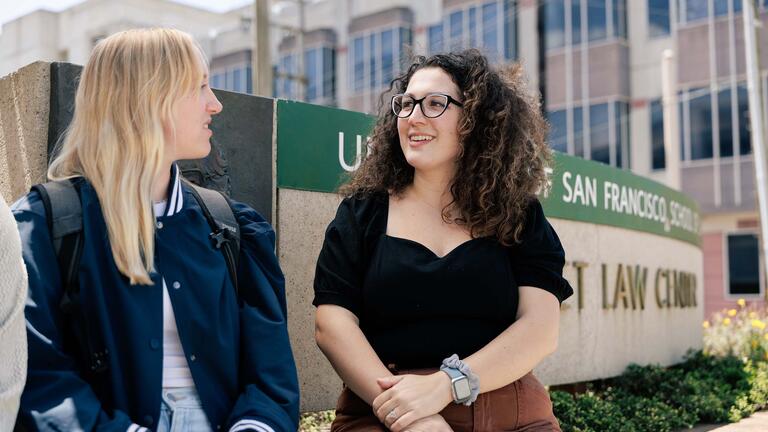 Two law students seated next to the USF School of Law sign