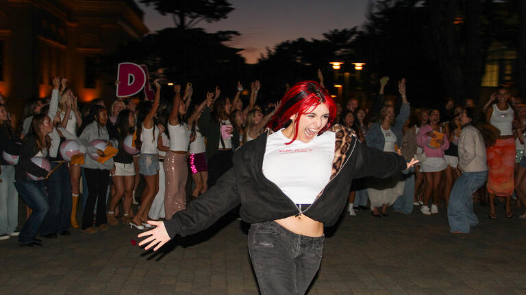 student runs with arms in the air with crowd jumping into the air behind them