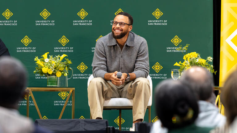 Steph Curry sits on stage and smiles at crowd at the Silk Speaker Series event