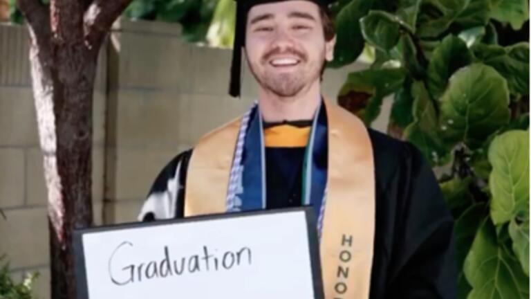 Shane Yoshiyama in graduation attire holding a sign that says Graduation Today!