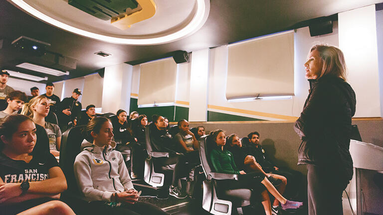 Coach Helen Lehman-Winters addresses athletes in auditorium