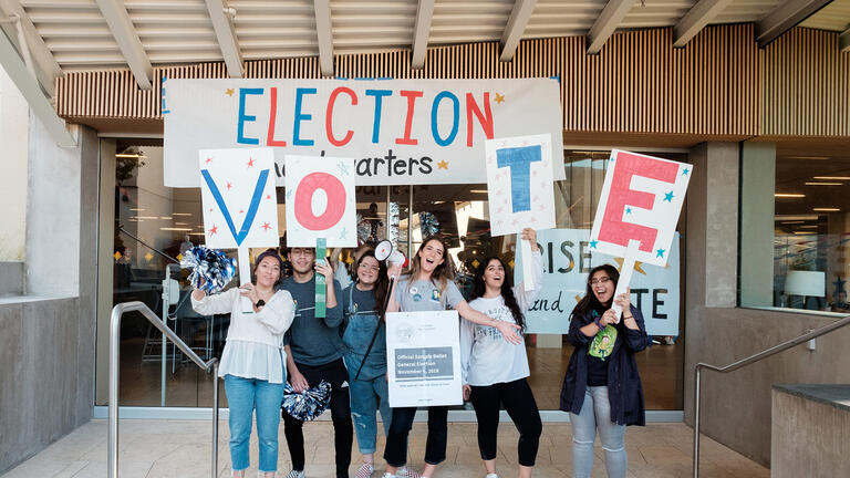 Students holding signs and talking into bullhorns, encouraging others to vote.