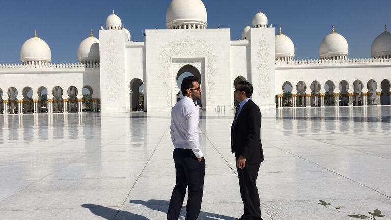 Two people stand in front of a mosque