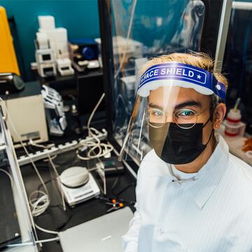 Lab associate in protective gear stands in front of lab equipment