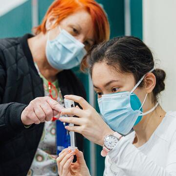 Registered nurse supervises nursing student filling syringe from vial