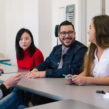 A group of students at a table speak to their professor.