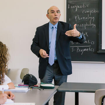 Teacher lectures from the front of a classroom.