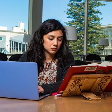 Student studies with a book and a laptop in the library.