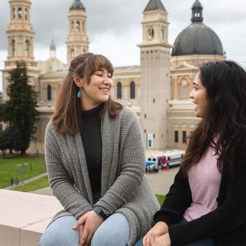 Two students chat while sitting on a wall.