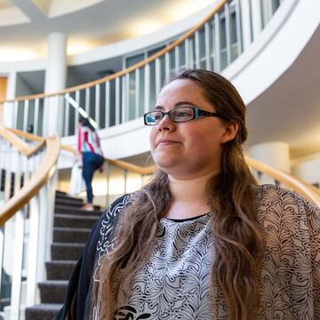 Student stands in the atrium lobby with stairs behind.