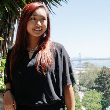 Student stands on a hill with the city and bay visible behind.