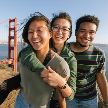 Students hug and laugh on a hill overlook for the Golden Gate Bridge.