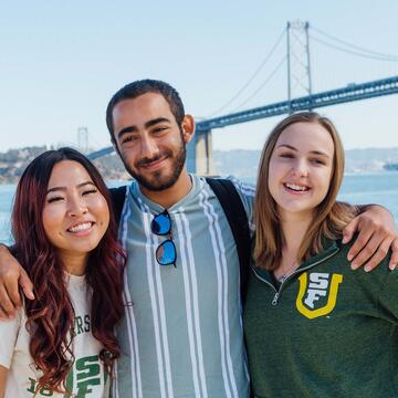 Three students pose in front of the Bay Bridge.