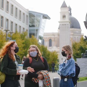 Three students talk on lower campus with the church in the background.