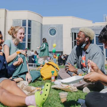 Four students chat and eat lunch on the grass.