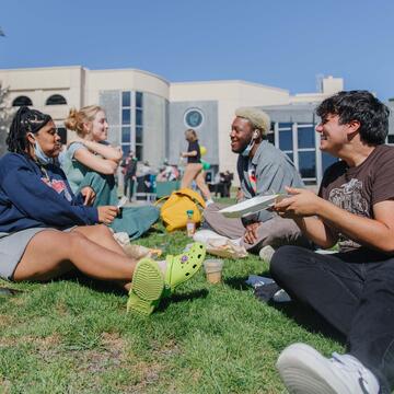Students eat lunch and laugh on the lawn.