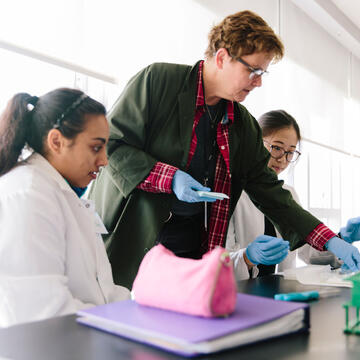 Professor assists students working at a table in a Biology lab.