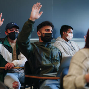 A group of students in class, two with their hands raised.