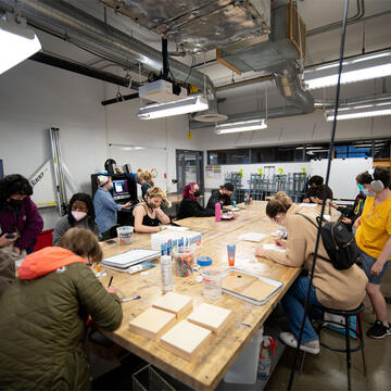 Students work on art projects at a large table in class.
