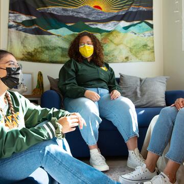 Three students chat in a dorm room.