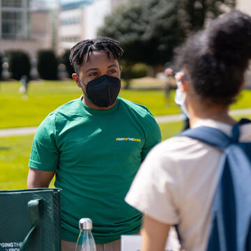 Staff member speaks to a student at an information table on the lawn.